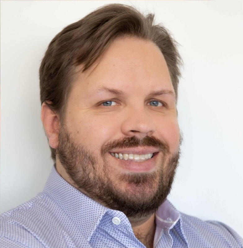 Brett Deister, host of Digital Coffee, smiling in a light blue patterned shirt